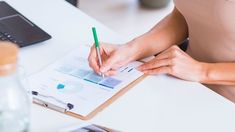 a woman sitting at a desk writing on a piece of paper with a pencil in her hand