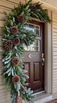 a wreath with pine cones and evergreen leaves on the front door porch for christmas time