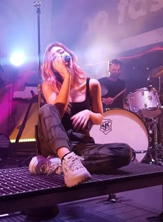 a woman sitting on top of a table next to a drum set and microphone in front of her