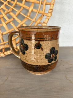 a brown and black coffee cup sitting on top of a wooden table next to a wicker basket