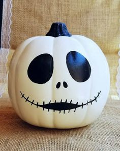 a white pumpkin decorated with black eyes and a skull on it's side, sitting on a burlap surface