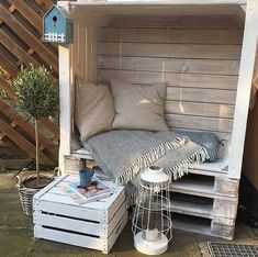 a bench made out of pallets with pillows and blankets on the seat, next to a potted plant