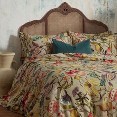 a bed with a floral comforter and pillows on it in front of a blue wall