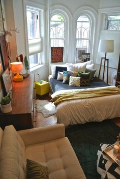 a living room filled with lots of furniture next to two large windows and a bed