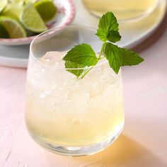 a glass filled with lemonade and limes on top of a pink table cloth