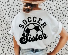 a woman wearing a white shirt with the word soccer sister on it and a black soccer ball