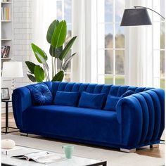 a blue couch sitting in front of a window next to a table with a potted plant