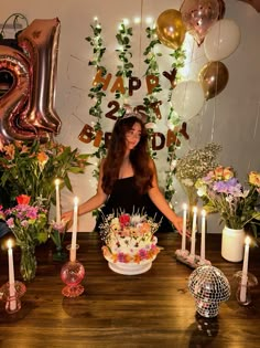 a woman sitting in front of a birthday cake surrounded by balloons and flowers with candles