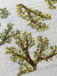 an embroidered piece of cloth with green and yellow leaves on it, in the shape of a tree