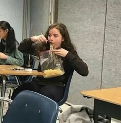 two women sitting at a table eating food and drinking from their cups in front of them