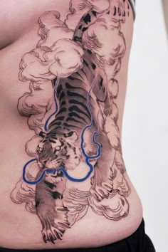 a woman's stomach with a tiger tattoo on the side and clouds in the background