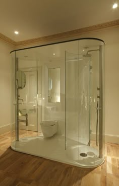 a bathroom with a glass shower stall and toilet in the corner, on wooden flooring