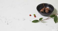 two small berries in a black bowl on a marble counter top next to some green leaves