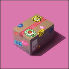 a cardboard box with stickers on it sitting on top of a pink surface in front of a purple background