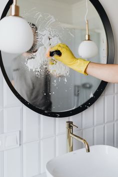 a person in yellow gloves cleaning a bathroom mirror