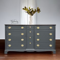 a grey dresser with gold handles and knobs on the doors is in front of a window