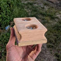 a hand holding a wooden box with two holes in the front and one hole in the back