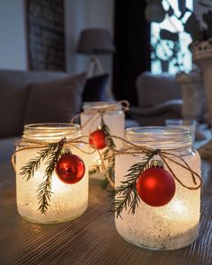 three mason jars filled with christmas ornaments on top of a wooden table next to candles