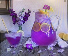 a pitcher filled with purple liquid next to a vase full of lemons and flowers