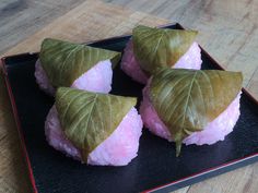 four pieces of sushi on a black plate with leafy leaves and pink sauce