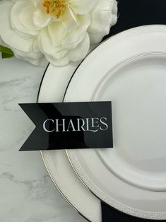 there is a place setting with plates and flowers on the table, along with a name plate