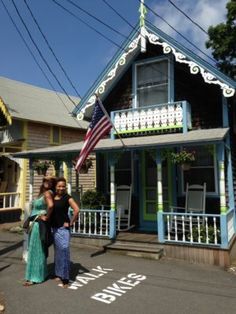 two women are standing in front of a house with an american flag on it's roof