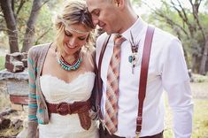 a man and woman standing next to each other in front of trees wearing suspenders