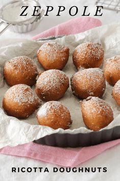 powdered sugar covered doughnuts in a pan on a pink towel next to a cupcake tin