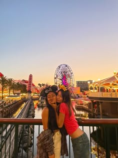 two women standing next to each other in front of a ferris wheel at an amusement park