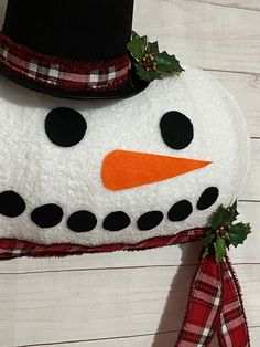 a snowman with a black hat and plaid scarf hanging on a white wooden wall