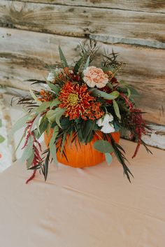 an arrangement of flowers and greenery in a pumpkin shaped vase on a tablecloth