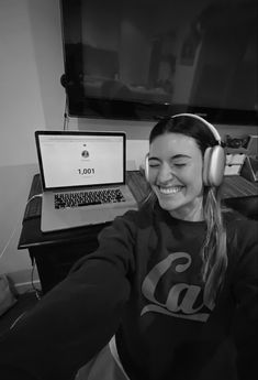 a woman wearing headphones sitting in front of a laptop computer and smiling at the camera