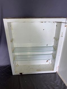 an empty white cabinet with glass shelves on the bottom and inside, against a purple wall