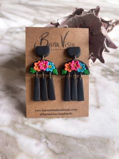 the earrings are decorated with colorful flowers and black plastic beads, on top of a card