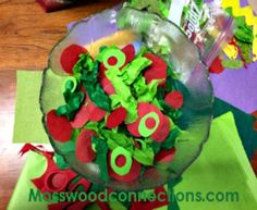 a glass bowl filled with green and red paper flowers on top of a wooden table