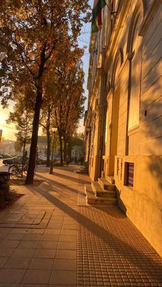 the sun shines on an empty sidewalk in front of a row of buildings and trees