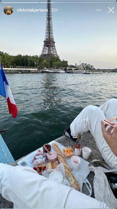 two people sitting on a boat eating food in front of the eiffel tower