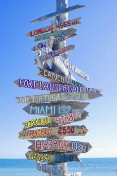 a wooden sign post with many different signs on it's side in front of the ocean