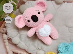 a crocheted pink teddy bear laying on top of a white blanket next to other stuffed animals