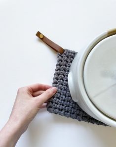 a hand is holding the handle of a crocheted dishcloth with a wooden spoon in it