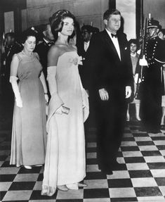 an old black and white photo of two people in formal wear walking down the hall