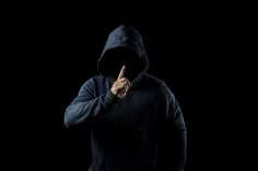 a man in a black hoodie making the peace sign with his hand while standing against a black background