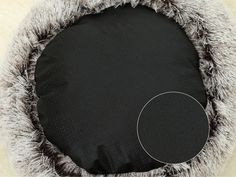 a black and white dog bed with grey fur on it's sides, next to a round pillow