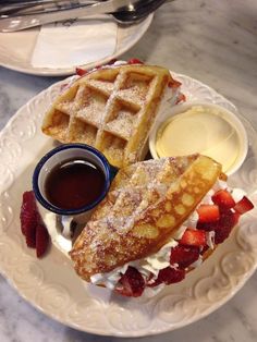 two waffles on a plate with syrup and strawberries next to each other