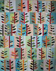 a quilt made with leaves and strips on the front, in blue, pink, green, orange and white colors