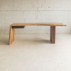 a wooden bench sitting on top of a white floor next to a brick wall in an empty room