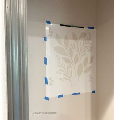 a white wall with blue tape on it and a flower stencil taped to the wall