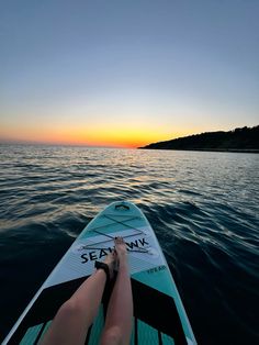 a person laying on top of a surfboard in the middle of water at sunset