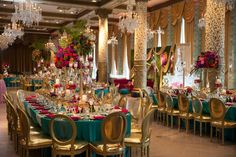 a banquet hall with tables and chairs covered in blue cloths, gold trimmings and chandeliers