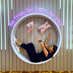 a woman laying in a round white chair with pillows on the wall and neon lights above her